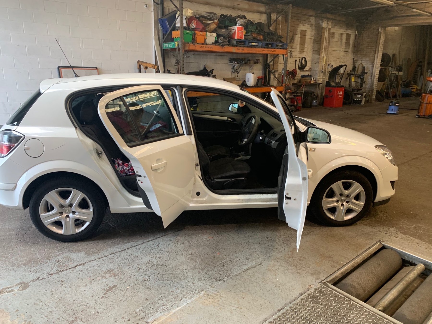 A white Vauxhall Astra in the workshop with its doors open, standing over the brake rollers
