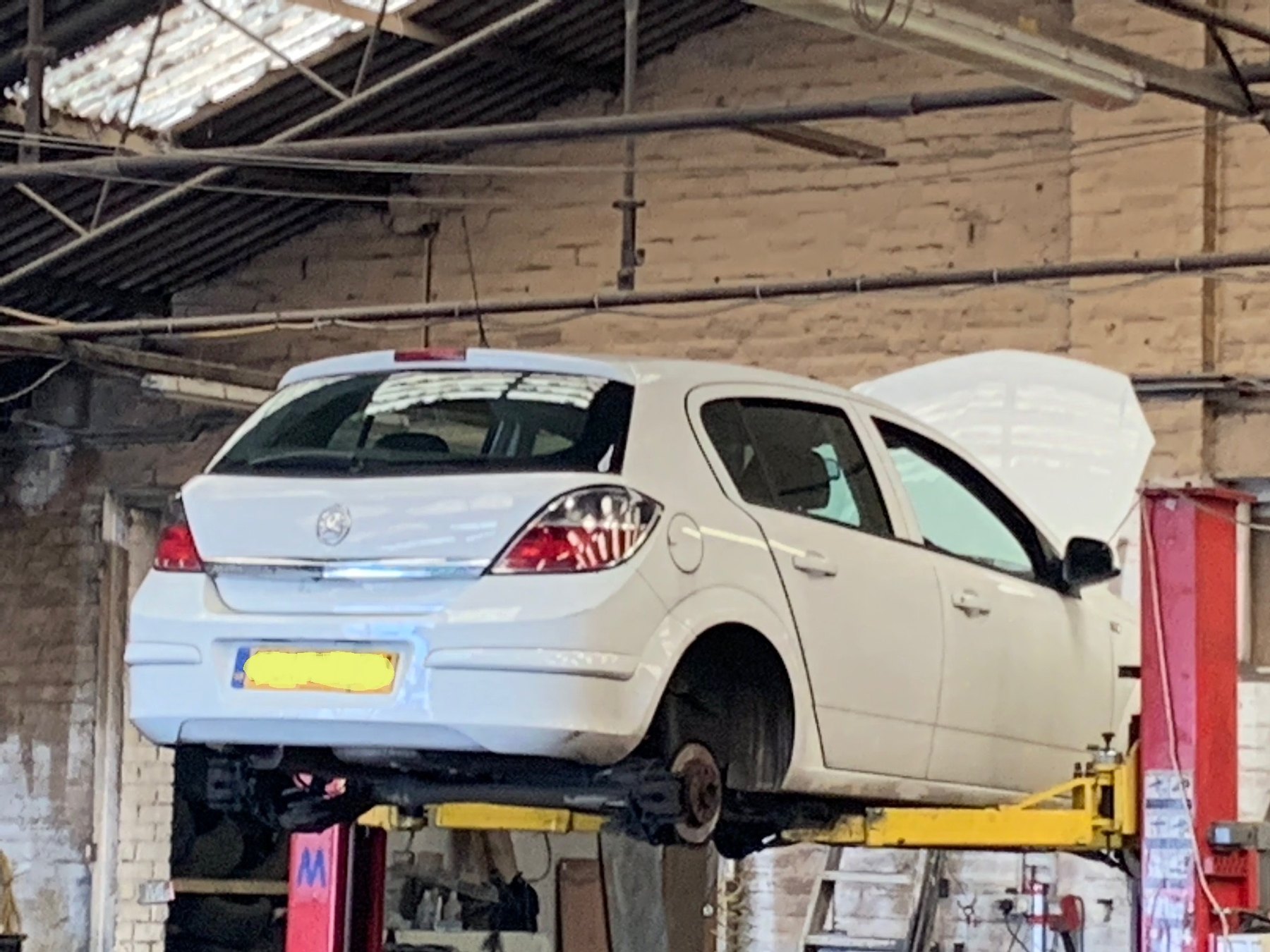 The white Astra raised on a red two-post ramp with its bonnet up