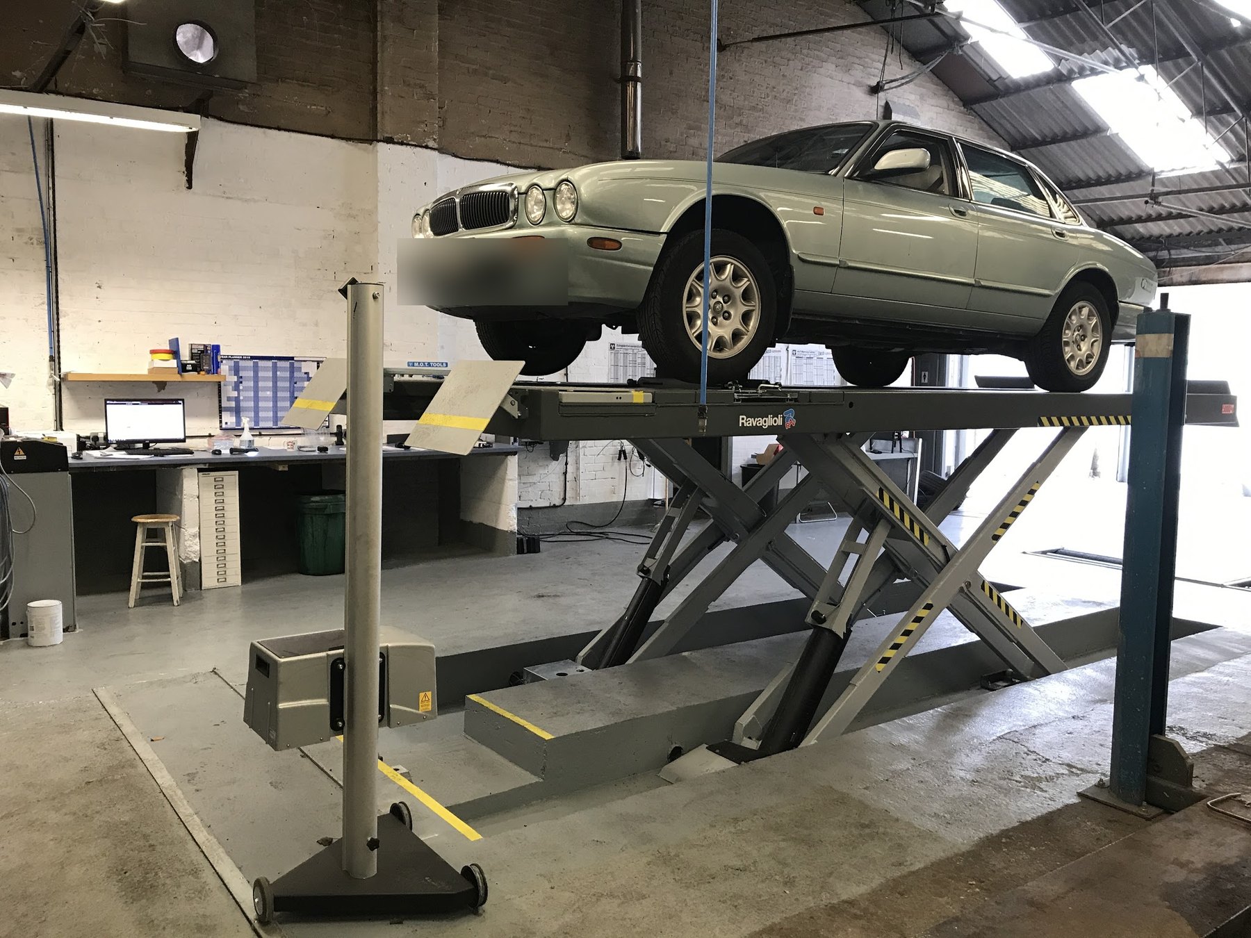 A pale green Jaguar saloon raised on the scissor lift inside the workshop